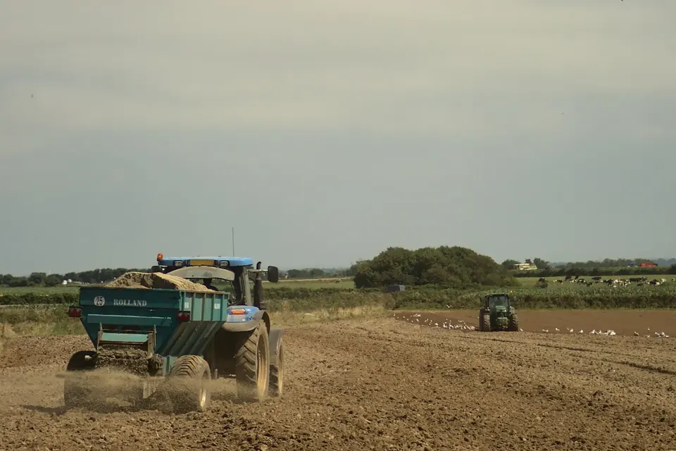 Deux tracteurs dans un champ labouré de Bretagne, l'un épandant un fertilisant, l'autre travaillant le sol derrière lui