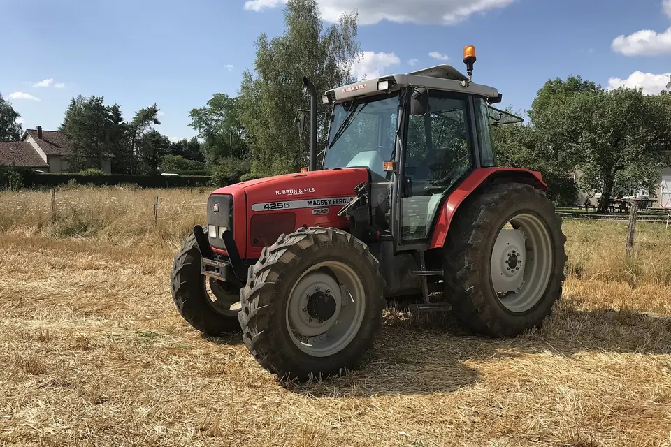 Tracteur rouge arrêté sur une parcelle de chaumes après un labour, sous un ciel bleu avec quelques nuages